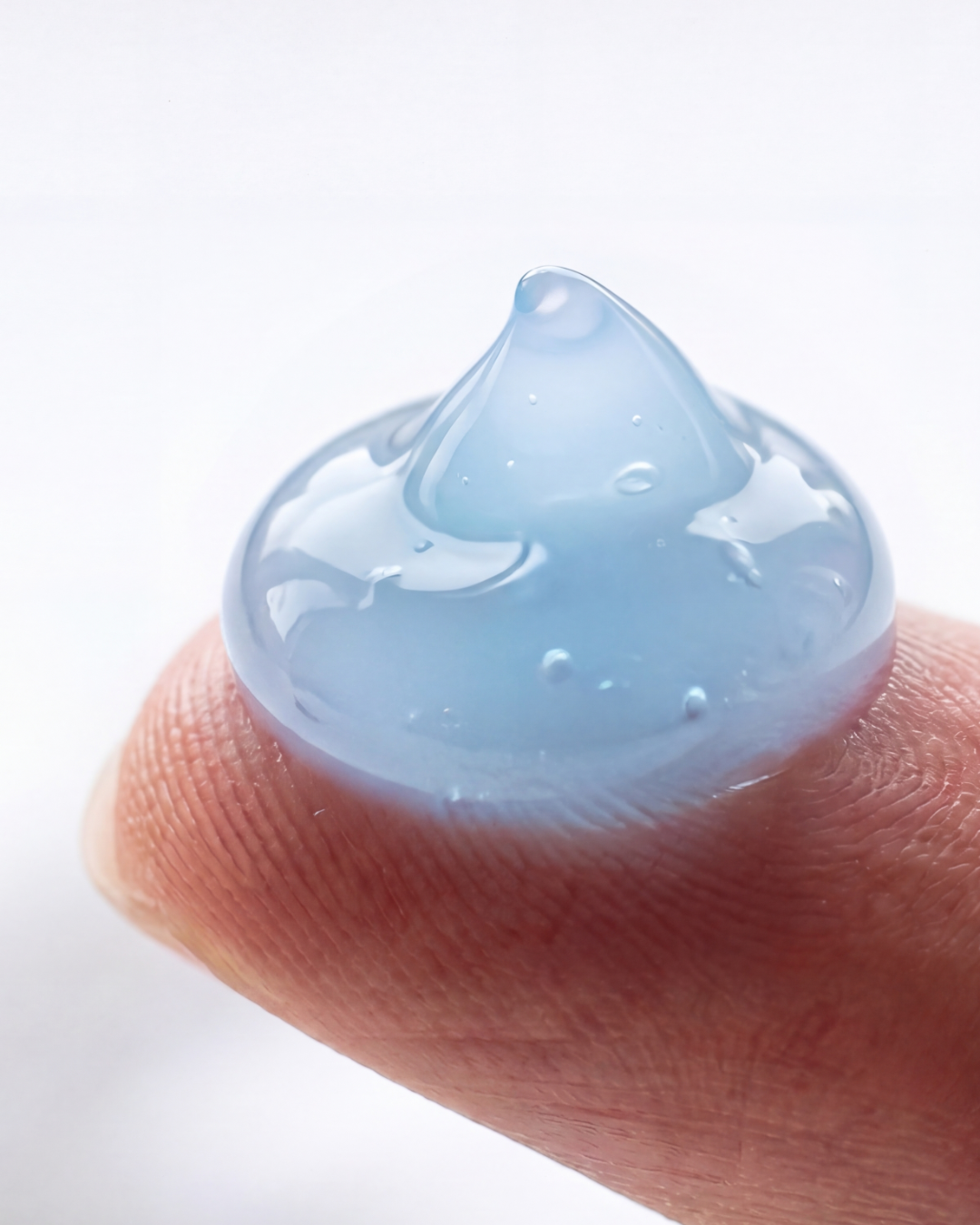 A bead of the blue Skin Normalizer gel on a fingertip — translucent copper-peptide blue holding a soft peak